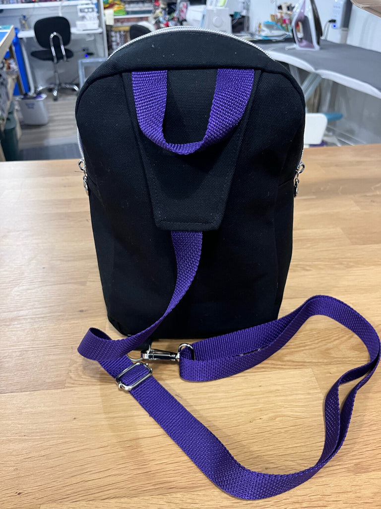 Back side of a black sling bag with purple straps
