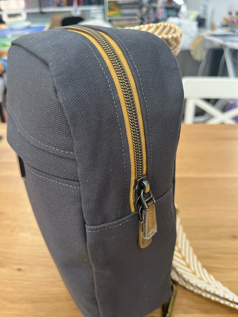 Close up of yellow and silver zipper on a dark grey Sling Bag