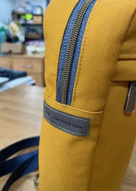 Mustard yellow sling bag with black strap close up of zipper